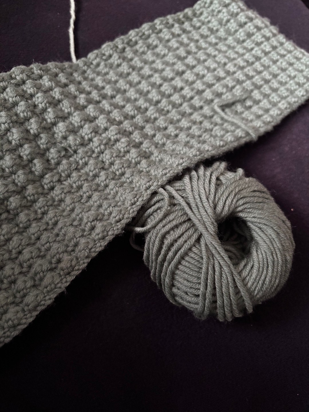 Graues Strickstück mit Strukturmuster neben einem grauen Garnknäuel