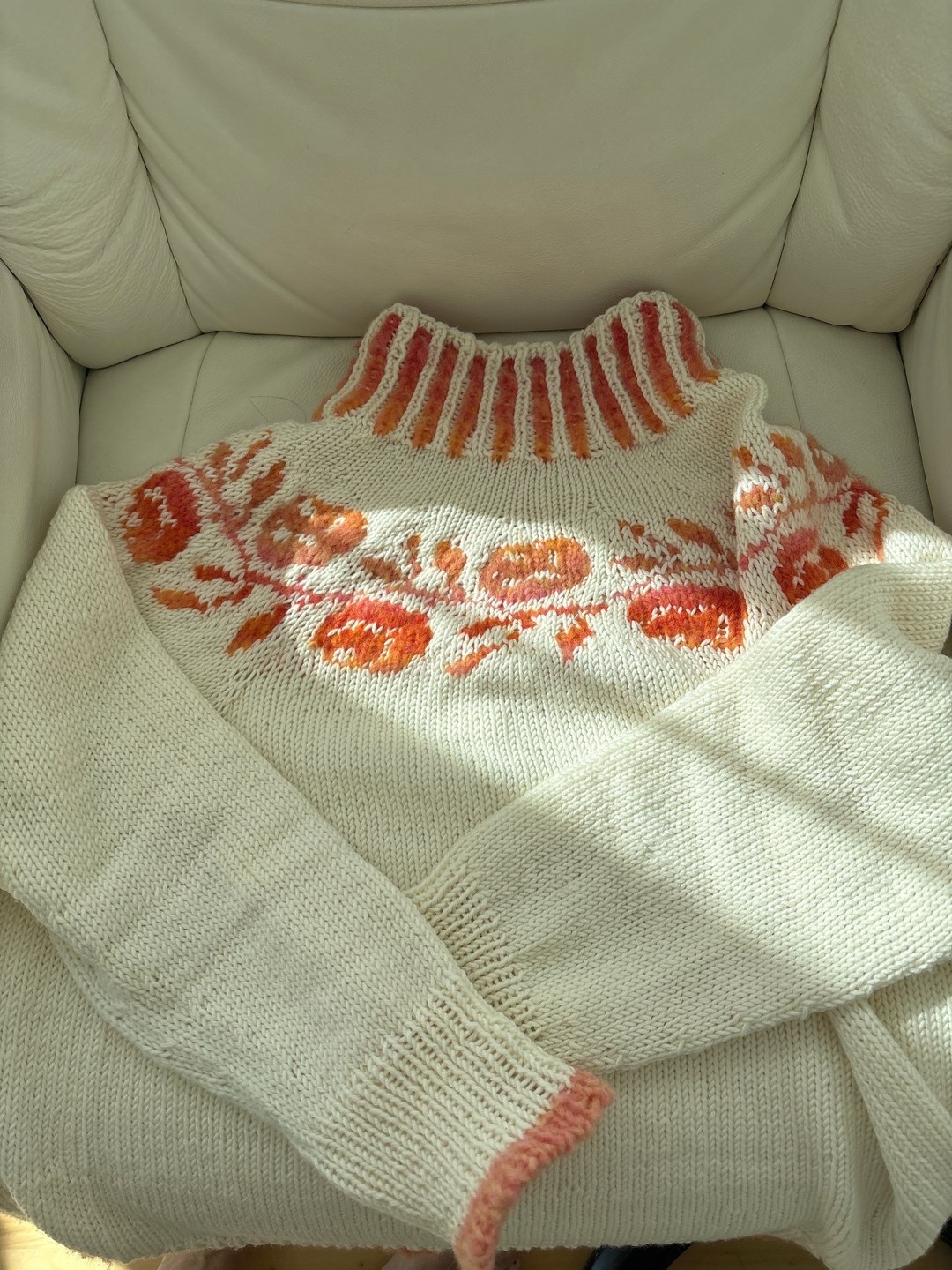 Weisser Strickpullover mit orangefarbenem Rundpassenmuster auf einem Sessel