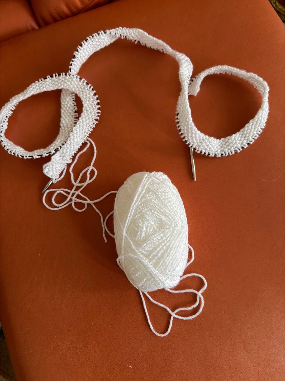 Zwei schmale weisse Strickbänder neben einem weissen Garnknäuel