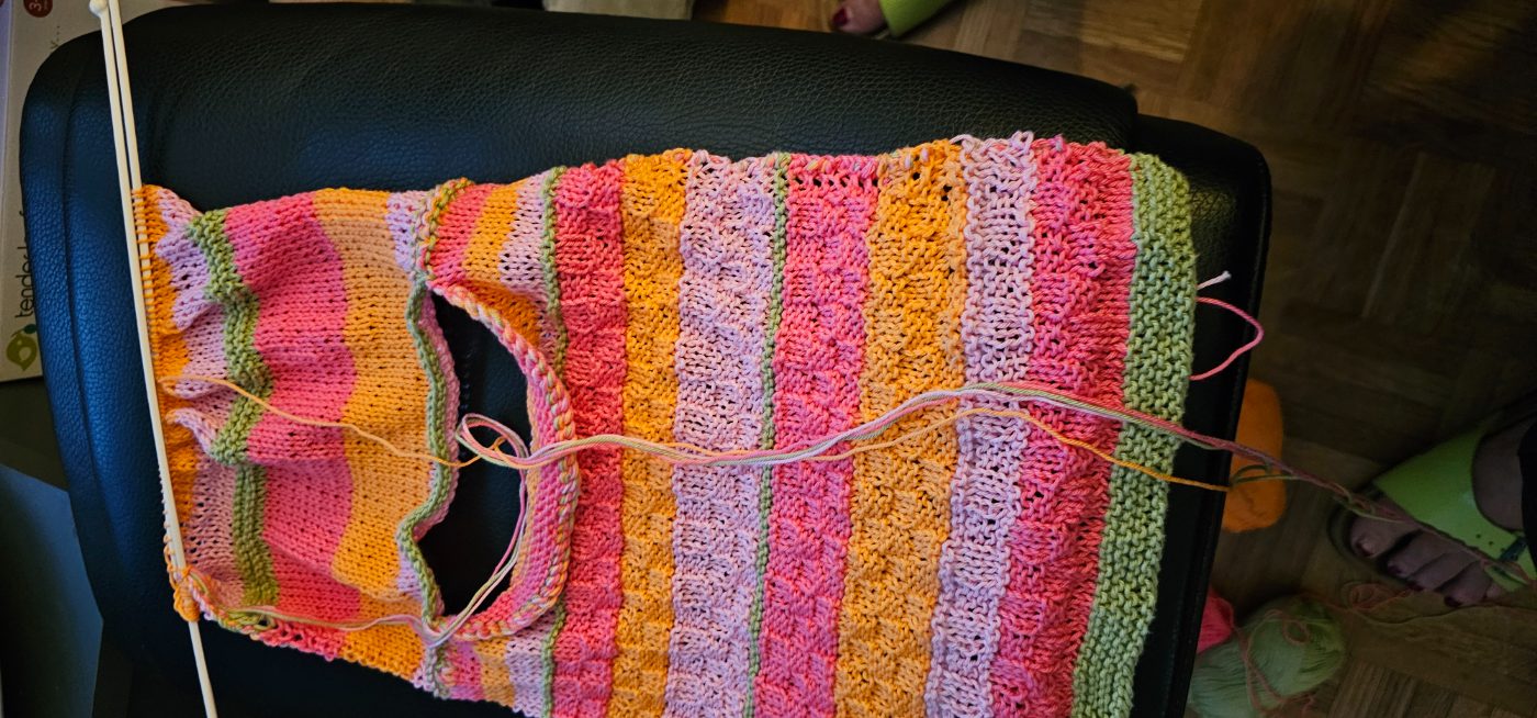 Ein bunt gestreifter Kinderpullover, noch auf den Nadeln