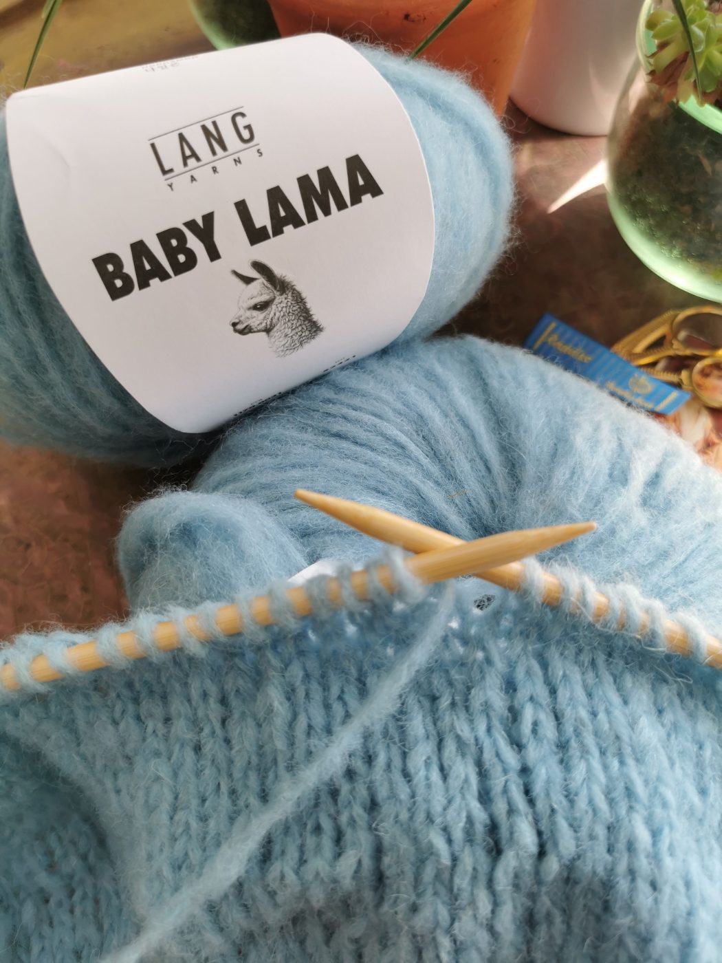 Hellblaues Garn auf den Nadeln, daneben die Banderole LANG YARNS Baby Lama