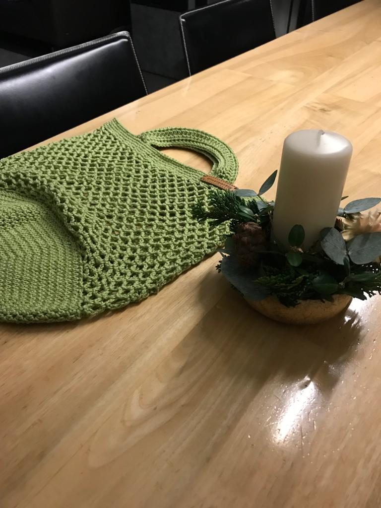Grüne gehäkelte Tasche neben einer Kerze